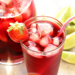 Hibiscus tea in glass and pitcher with limes next to it.