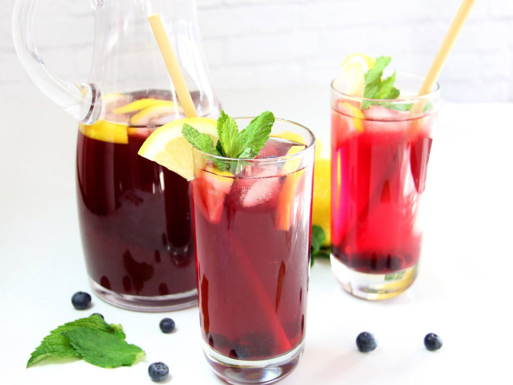 Homemade Blueberry Iced Tea in glasses with lemon slices, mint leaves, and blueberries alongside pitcher