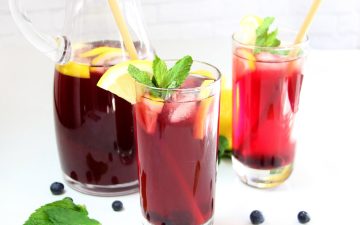 Homemade Blueberry Iced Tea in glasses with lemon slices, mint leaves, and blueberries alongside pitcher