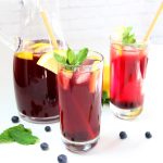 Homemade Blueberry Iced Tea in glasses with lemon slices, mint leaves, and blueberries alongside pitcher