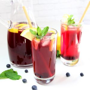 Homemade Blueberry Iced Tea in glasses with lemon slices, mint leaves, and blueberries alongside pitcher