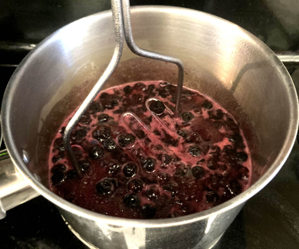 Mashing blueberries with potato masher for a blueberry simple syrup