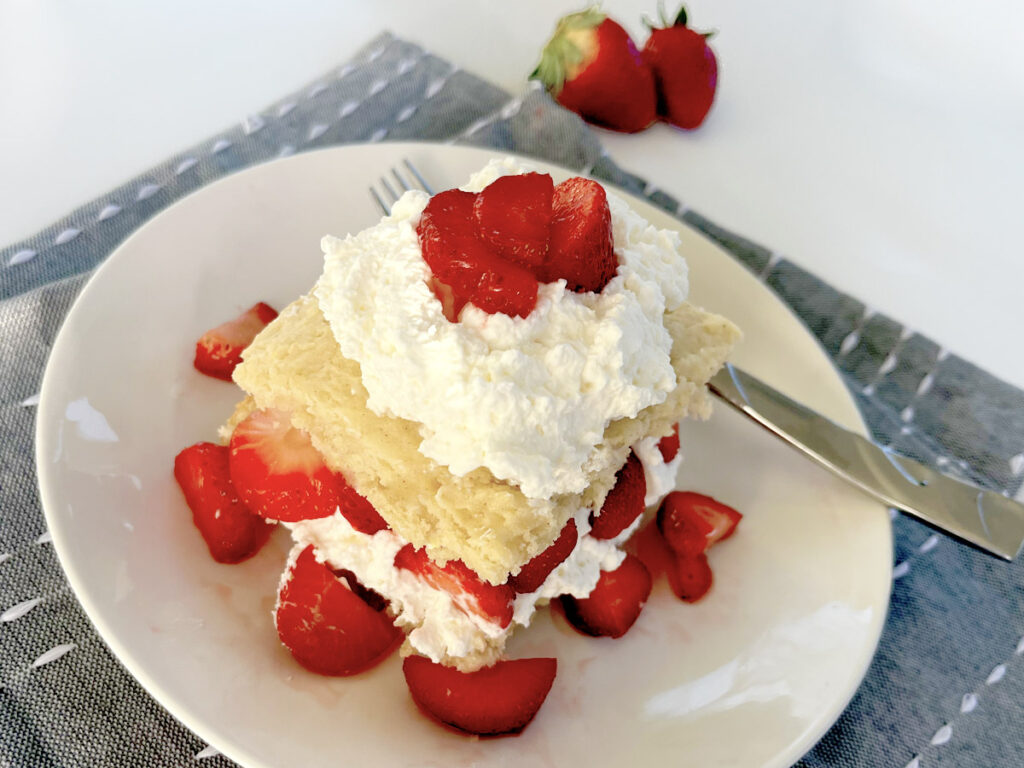 Gluten Free Strawberry Shortcake on plate with blue napkin and layers of cream and strawberries.