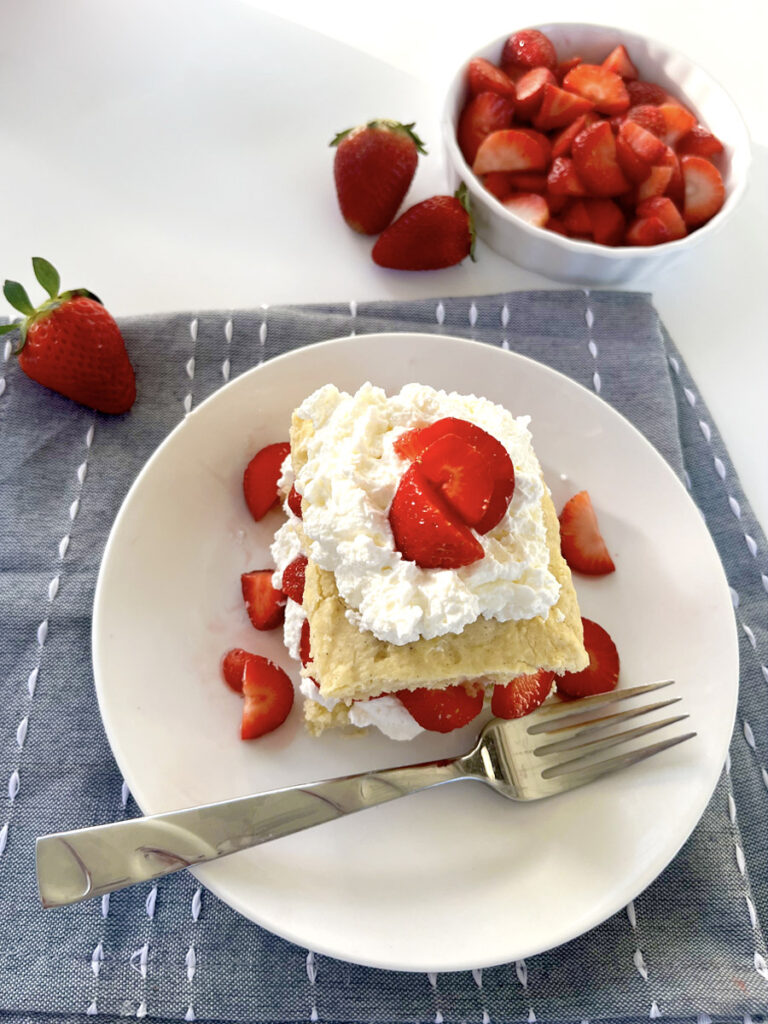Gluten Free Strawberry Shortcake on plate with blue napkin and layers of cream and strawberries.
