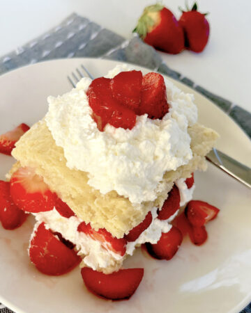 Gluten Free Strawberry Shortcake on plate with blue napkin and layers of cream and strawberries.