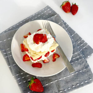 Gluten Free Strawberry Shortcake on plate with blue napkin and layers of cream and strawberries.