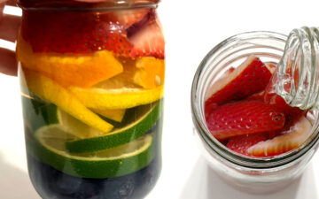 Fruit infused vodka with rainbow fruits alongside of vodka being poured into a mason jar full of strawberries