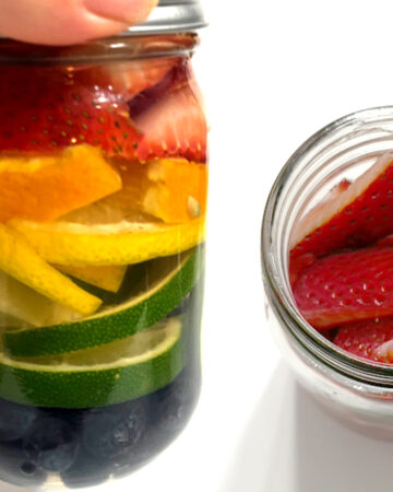 Fruit infused vodka with rainbow fruits alongside of vodka being poured into a mason jar full of strawberries
