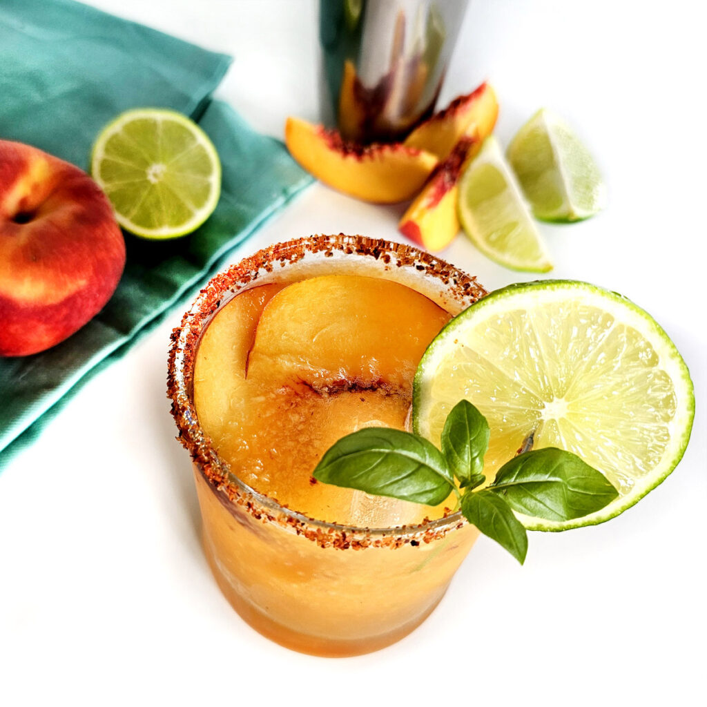 Hot Honey Peach Margarita and peach slices and blue napkin and limes