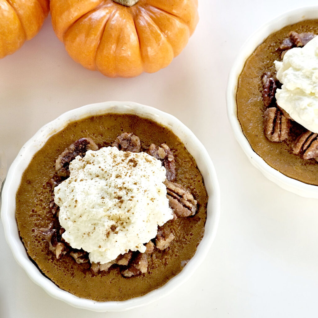 Pumpkin custard with caramelized pecans, whipped cream, and mini pumpkins in background