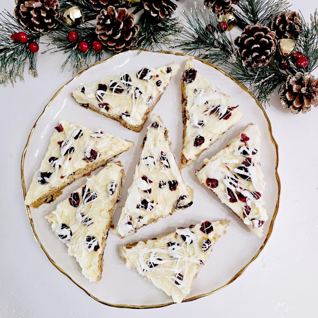 Gluten Free Cranberry Bliss Bars on Gold Framed White Plate with Sparkly Holiday Decorations Around It