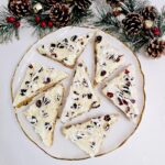 Gluten Free Cranberry Bliss Bars on Gold Framed White Plate with Sparkly Holiday Decorations Around It