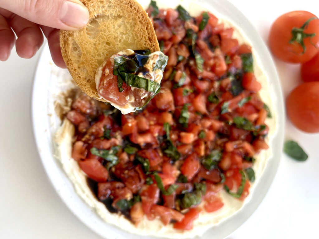 Bruschetta Dip with a crostini being dipped