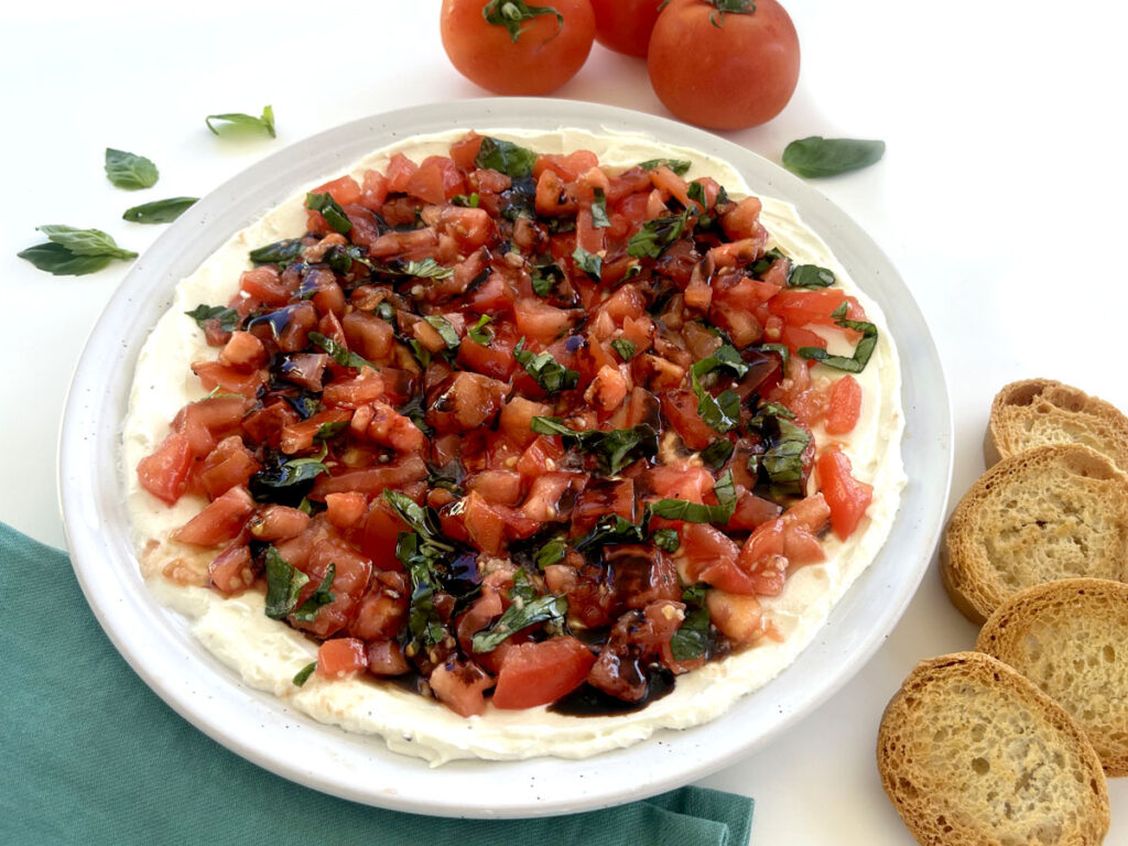 Bruschetta Dip next to tomatoes, basil, and crostinis