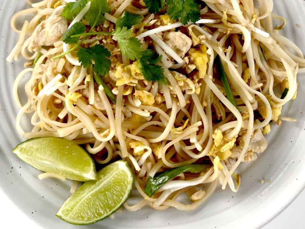 Gluten Free Pad Thai on white plate garnished with limes and crushed peanuts and cilantro