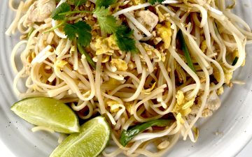 Gluten Free Pad Thai on white plate garnished with limes and crushed peanuts and cilantro