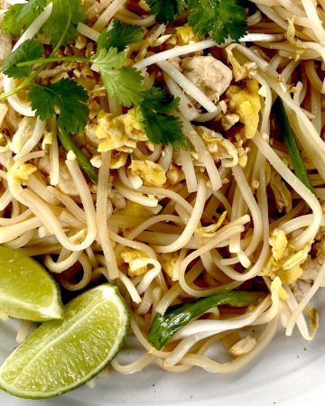 Gluten Free Pad Thai on white plate garnished with limes and crushed peanuts and cilantro
