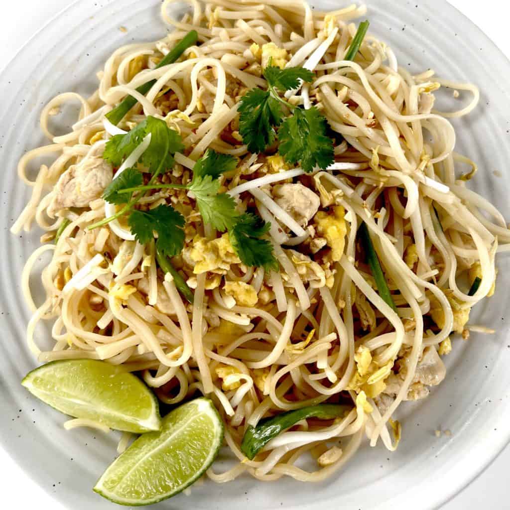 Gluten Free Pad Thai on white plate garnished with limes and crushed peanuts and cilantro