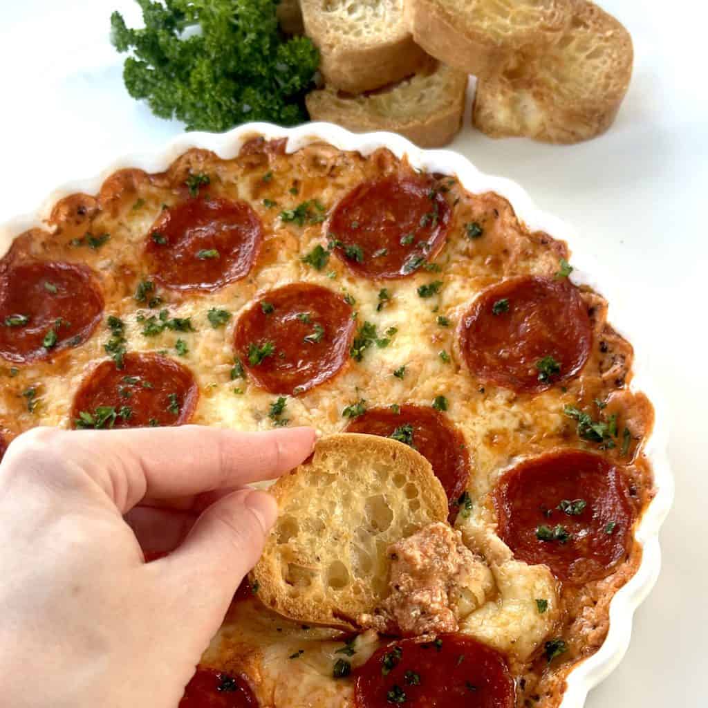 Pizza Dip in Round White Dish, with crostinis dipped in. Next to parsley