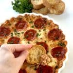 Pizza Dip in Round White Dish, with crostinis dipped in. Next to parsley