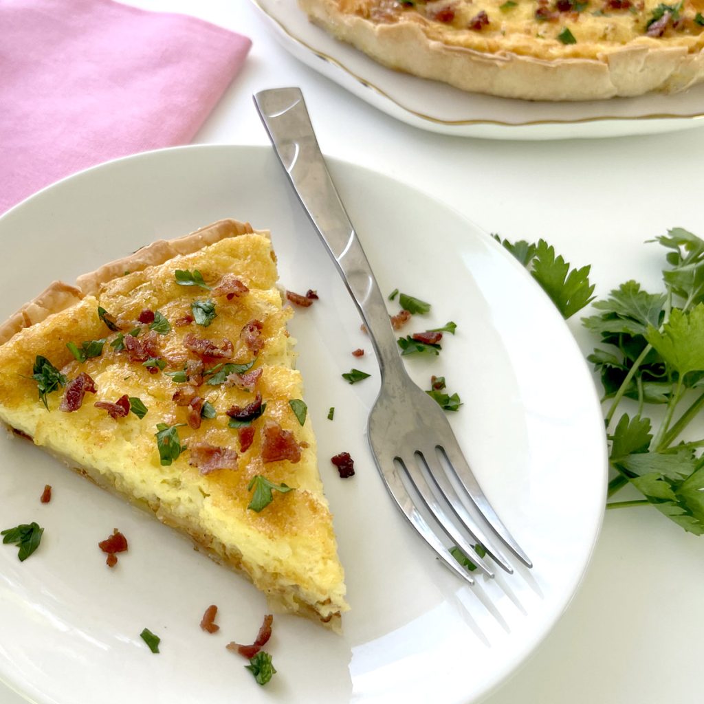 Gluten Free Quiche Lorraine on plate with parsley and quiche plate next to it and pink napkin