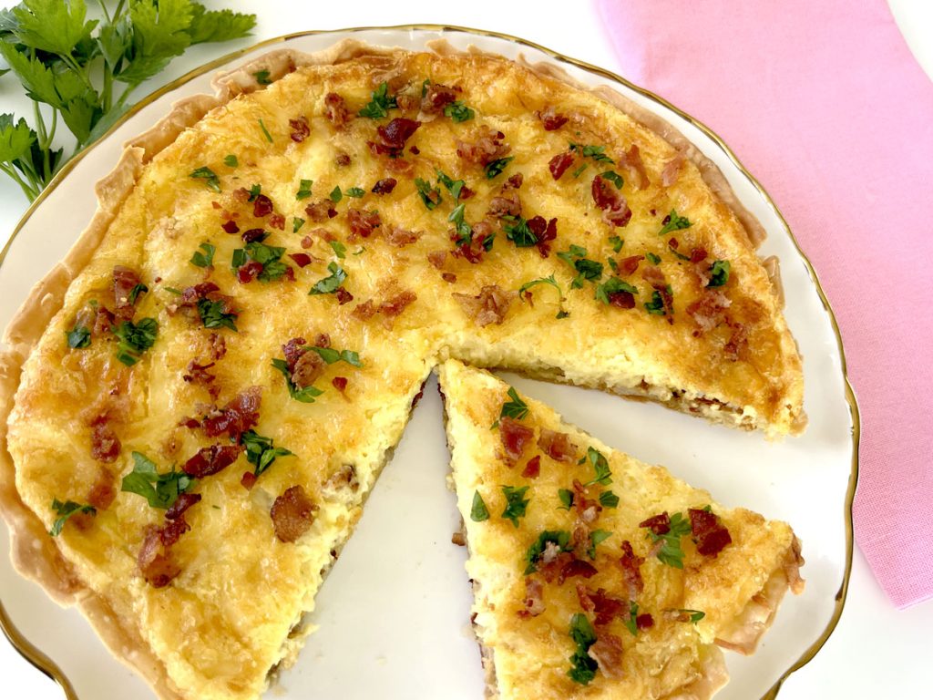 Gluten Free Quiche Lorraine on plate with parsley and quiche plate next to it and pink napkin