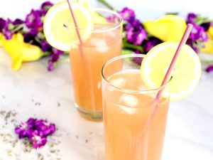 Lavender Lemonade Cocktails in high ball glasses with purple and yellow flowers in background
