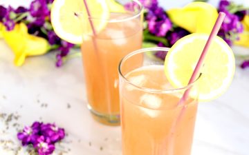 Lavender Lemonade Cocktails in high ball glasses with purple and yellow flowers in background