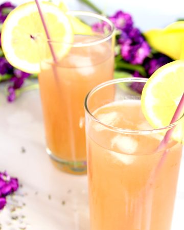 Lavender Lemonade Cocktails in high ball glasses with purple and yellow flowers in background