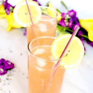 Lavender Lemonade Cocktails in high ball glasses with purple and yellow flowers in background close up