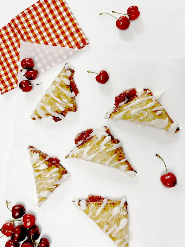 Gluten Free Cherry Turnovers on white parchment paper next to cherries