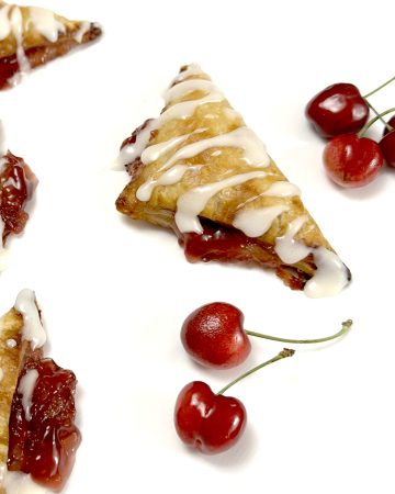 Gluten Free Cherry Turnovers on white parchment paper next to cherries