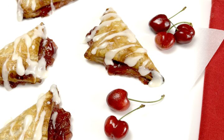 Gluten Free Cherry Turnovers on white parchment paper next to cherries
