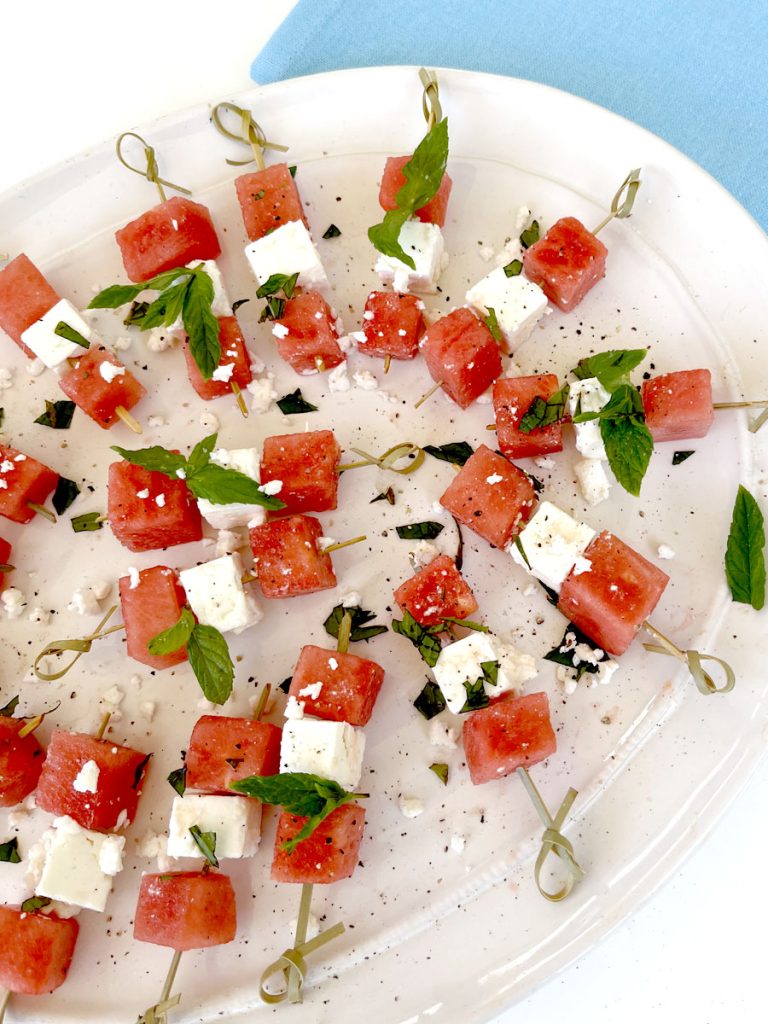 Watermelon Basil Feta Skewers on White Platter with Bright Blue Background