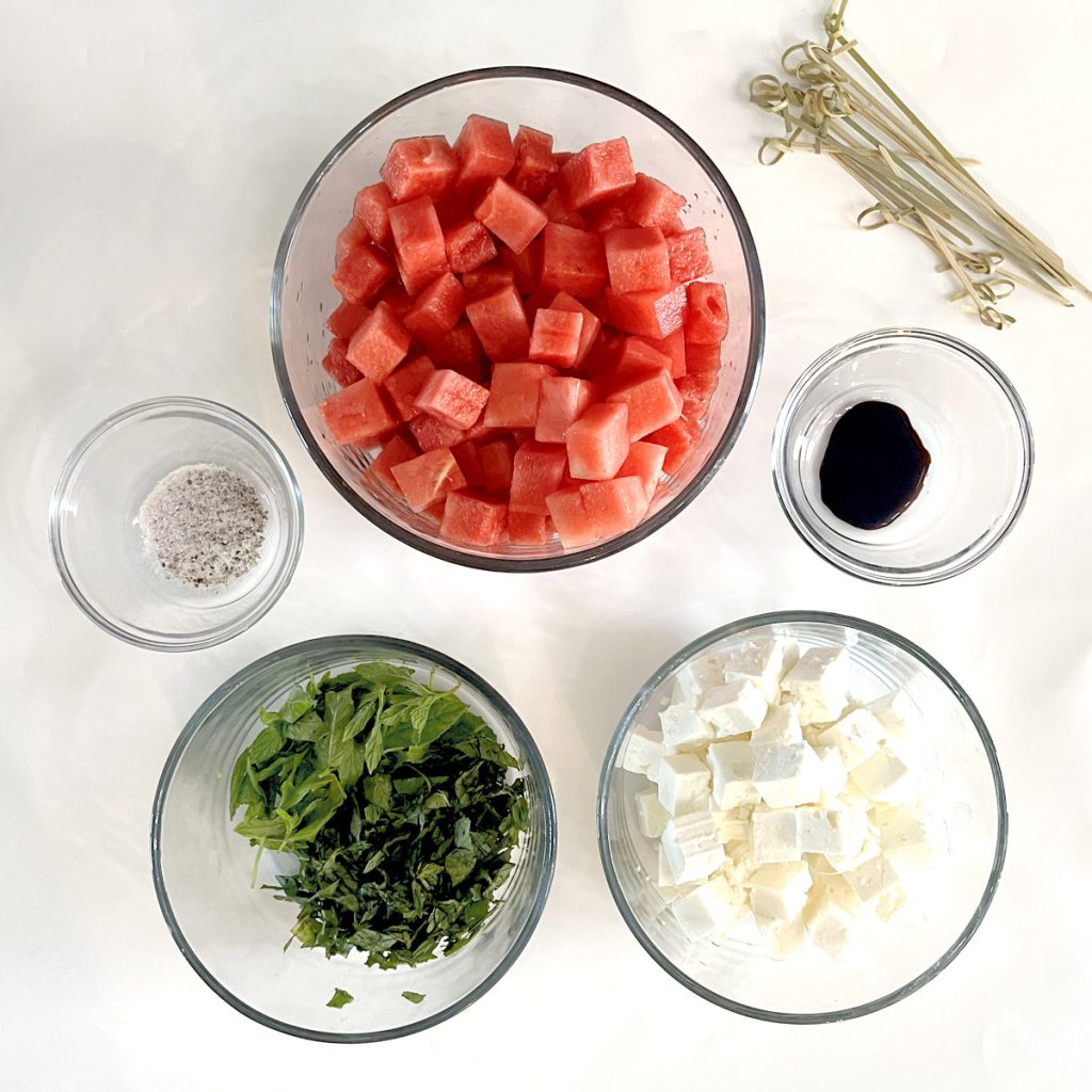 Watermelon Basil Feta Skewers on White Platter with Bright Blue Background Ingredients