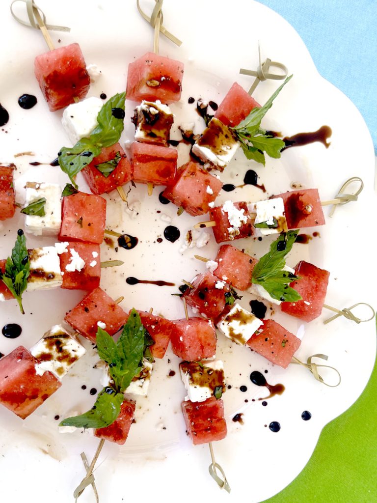 Watermelon Basil Feta Skewers on White Platter with Bright Blue and Green Background